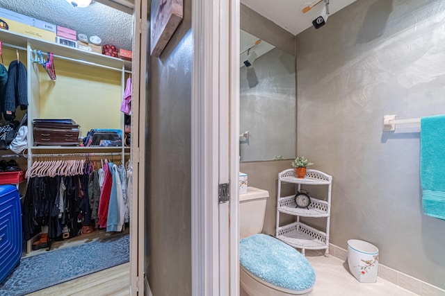 bathroom featuring a walk in closet, toilet, and baseboards