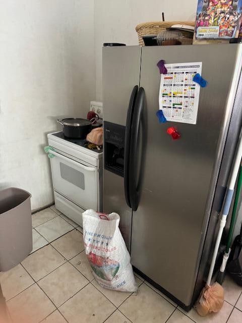 kitchen featuring light tile patterned floors, electric stove, and stainless steel fridge