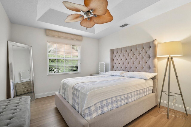 bedroom featuring ceiling fan, wood-type flooring, a textured ceiling, and a tray ceiling