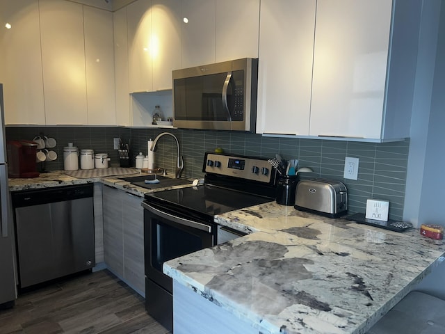 kitchen featuring light stone countertops, stainless steel appliances, and white cabinetry