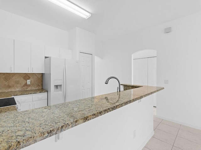 kitchen featuring light stone countertops, decorative backsplash, light tile patterned floors, white cabinets, and white fridge with ice dispenser