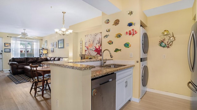 kitchen featuring dishwasher, hanging light fixtures, stacked washer / dryer, white cabinetry, and sink