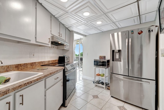 kitchen with coffered ceiling, sink, appliances with stainless steel finishes, light tile patterned flooring, and white cabinetry