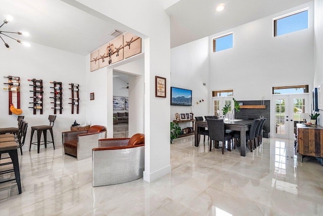 living room featuring a fireplace, an inviting chandelier, french doors, and a towering ceiling