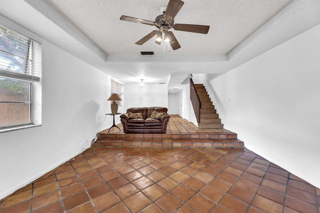 stairs featuring tile patterned floors, ceiling fan, a tray ceiling, and a textured ceiling