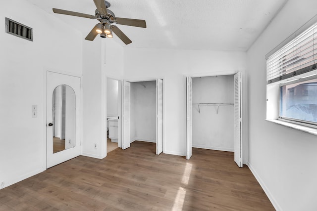 unfurnished bedroom featuring a textured ceiling, two closets, vaulted ceiling, ceiling fan, and dark hardwood / wood-style floors