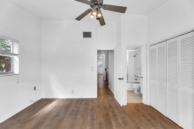 unfurnished bedroom with ensuite bath, ceiling fan, dark hardwood / wood-style floors, a towering ceiling, and a closet