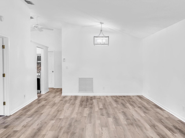 empty room featuring ceiling fan with notable chandelier, light hardwood / wood-style flooring, and high vaulted ceiling