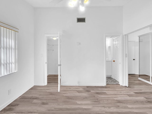 unfurnished bedroom featuring ensuite bathroom, a towering ceiling, light hardwood / wood-style flooring, a walk in closet, and a closet