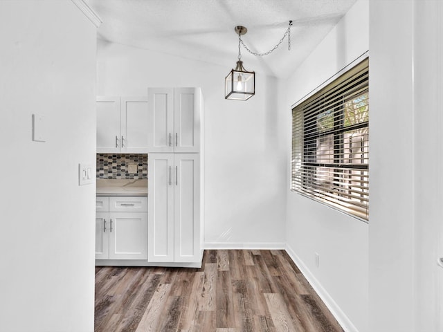 unfurnished dining area with wood-type flooring, a textured ceiling, and vaulted ceiling