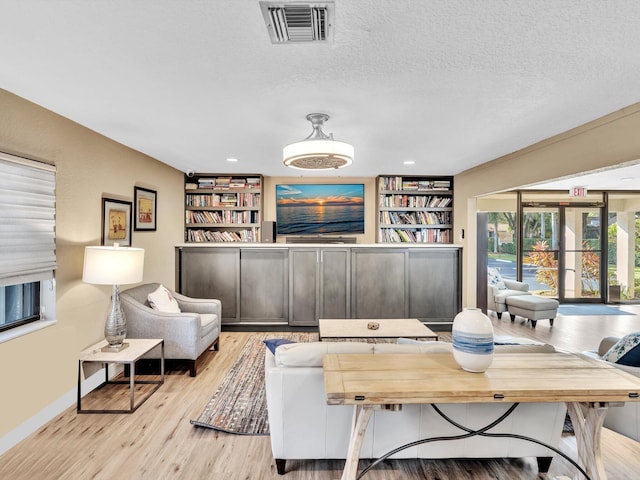 living room with built in shelves, a textured ceiling, and light hardwood / wood-style flooring