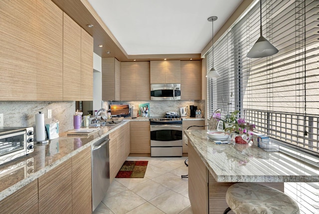 kitchen featuring sink, appliances with stainless steel finishes, light stone countertops, light tile patterned floors, and decorative light fixtures