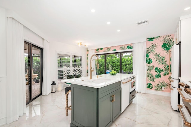 kitchen with white appliances, a center island with sink, a kitchen breakfast bar, green cabinets, and sink