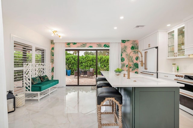 kitchen featuring range with electric cooktop, a kitchen breakfast bar, high end white refrigerator, a center island with sink, and white cabinets