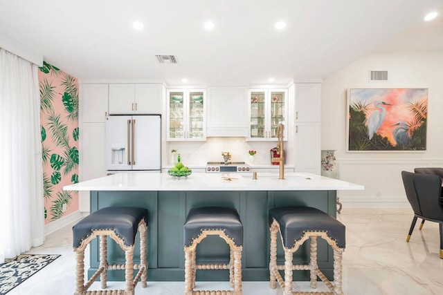 kitchen with a breakfast bar area, white cabinetry, high end fridge, and a center island with sink