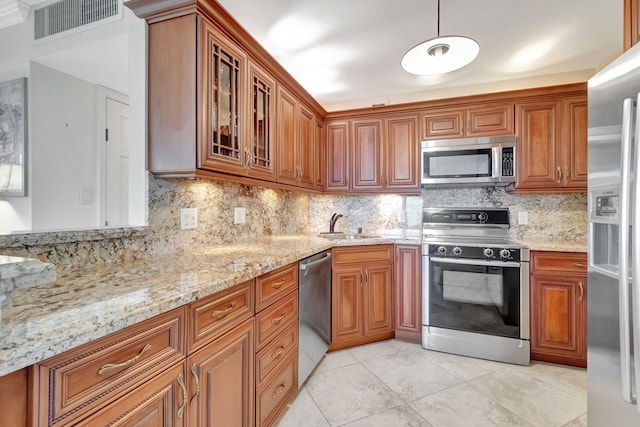 kitchen with tasteful backsplash, appliances with stainless steel finishes, decorative light fixtures, light stone countertops, and sink