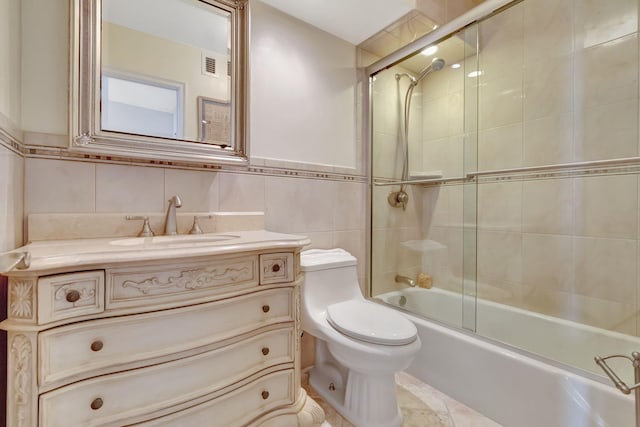 full bathroom featuring combined bath / shower with glass door, vanity, toilet, and tile walls