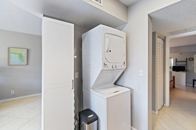 laundry room featuring stacked washing maching and dryer, a textured ceiling, and light tile patterned floors