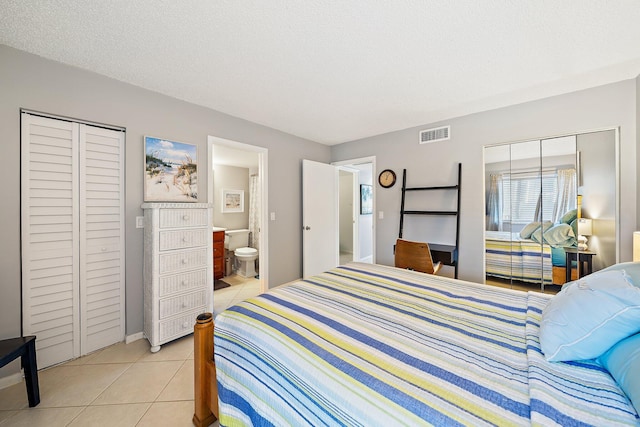 bedroom with ensuite bathroom, light tile patterned flooring, and a textured ceiling