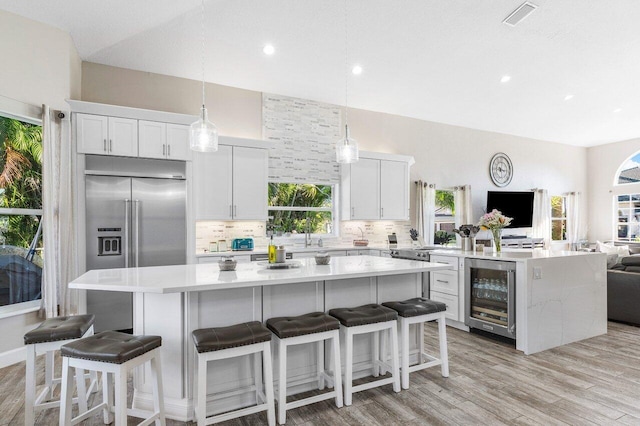 kitchen with beverage cooler, pendant lighting, a center island, light hardwood / wood-style floors, and white cabinetry