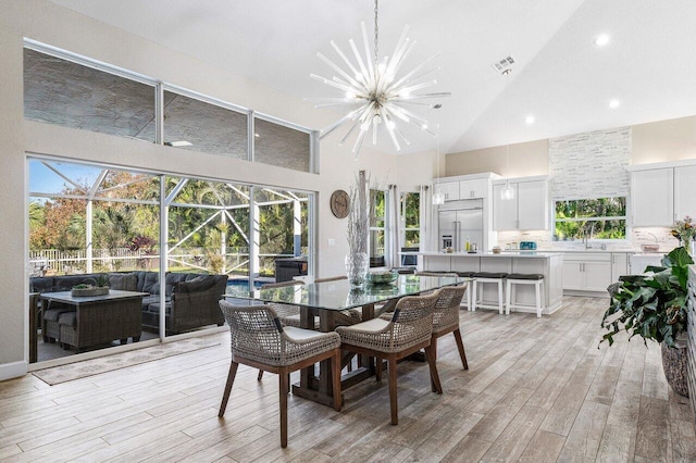 dining space with light hardwood / wood-style floors, high vaulted ceiling, and a notable chandelier