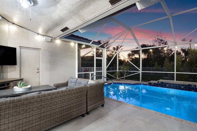 pool at dusk featuring glass enclosure, a patio area, and outdoor lounge area