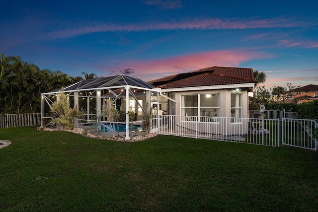 back house at dusk with glass enclosure, a fenced in pool, and a yard