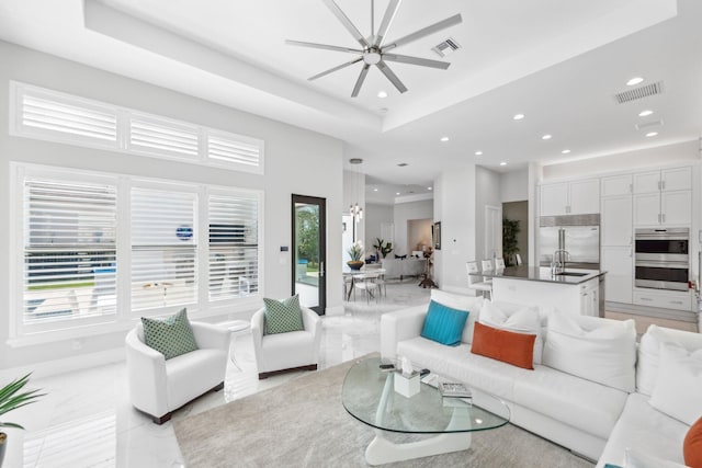 living room featuring ceiling fan, a raised ceiling, and sink