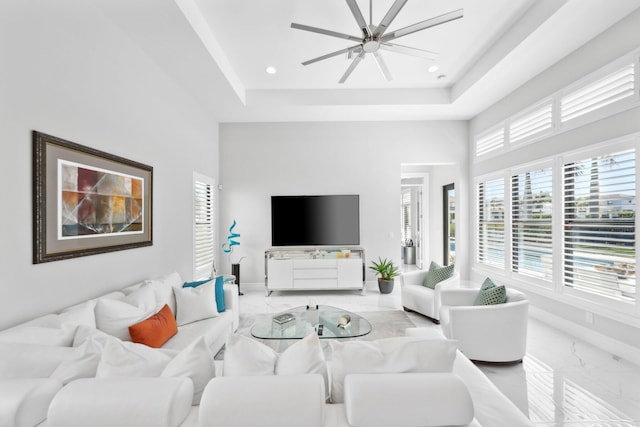 living room with a towering ceiling, a raised ceiling, and ceiling fan