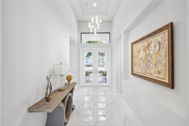 doorway to outside with a notable chandelier, a towering ceiling, french doors, and a raised ceiling