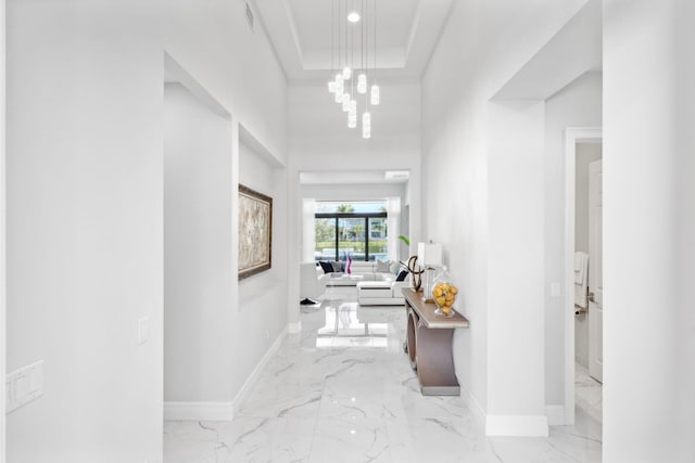 hall with a notable chandelier, a tray ceiling, and a high ceiling