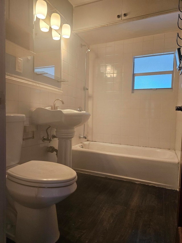 bathroom featuring tile walls, hardwood / wood-style floors, tiled shower / bath, and toilet