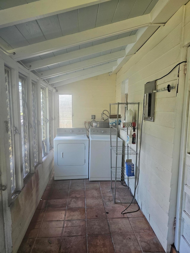 clothes washing area featuring electric panel, wood walls, and washer and clothes dryer