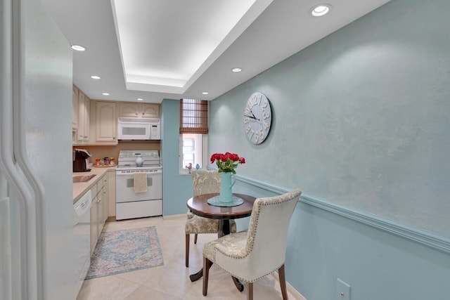 kitchen with light tile patterned floors, white appliances, a tray ceiling, and light brown cabinetry