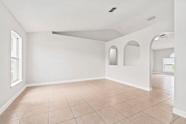 empty room featuring ceiling fan, vaulted ceiling, light tile patterned flooring, and a textured ceiling