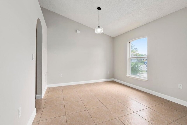 empty room featuring lofted ceiling, a textured ceiling, and light tile patterned floors