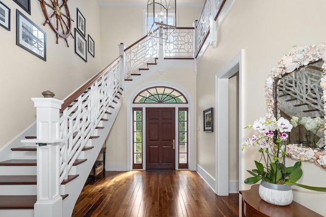 foyer featuring crown molding, wood-type flooring, a towering ceiling, and baseboards