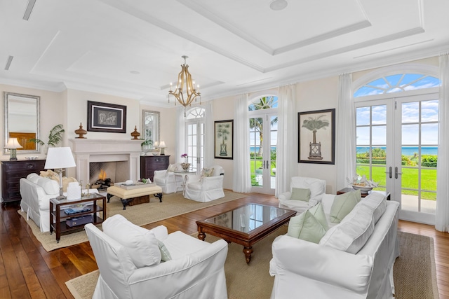 living room with a warm lit fireplace, dark wood-type flooring, french doors, ornamental molding, and a tray ceiling