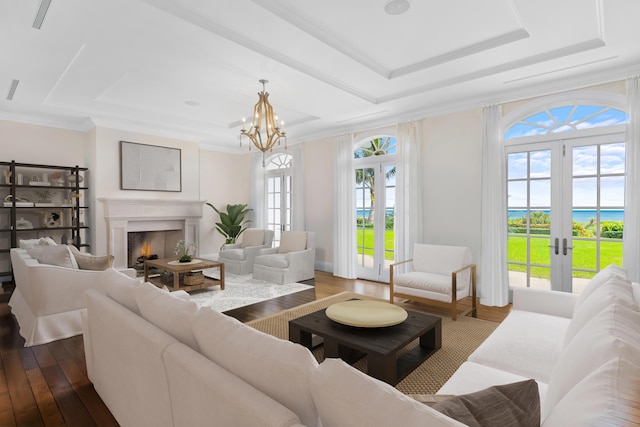 living area with dark wood finished floors, a lit fireplace, a tray ceiling, crown molding, and french doors