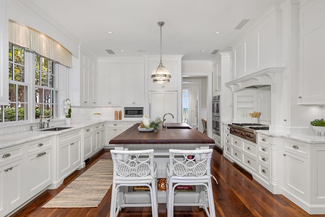 kitchen with a center island with sink, white cabinets, a sink, and built in appliances