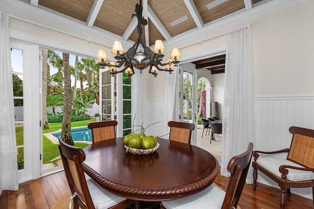 dining area with beam ceiling, hardwood / wood-style flooring, wainscoting, and an inviting chandelier