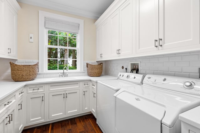 clothes washing area with cabinet space, ornamental molding, dark wood-type flooring, washing machine and dryer, and a sink