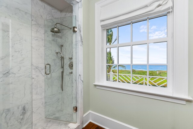 bathroom featuring a water view, a marble finish shower, and baseboards