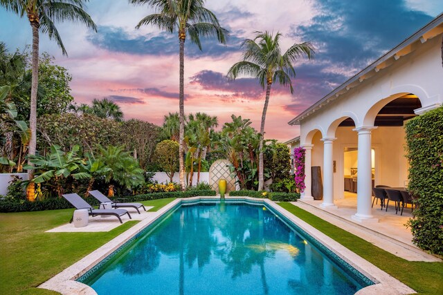 pool at dusk with a fenced in pool, a patio area, a lawn, and fence