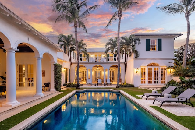 back house at dusk with a patio area, french doors, and a balcony