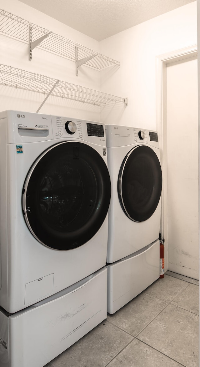 clothes washing area featuring washer and clothes dryer and light tile patterned flooring