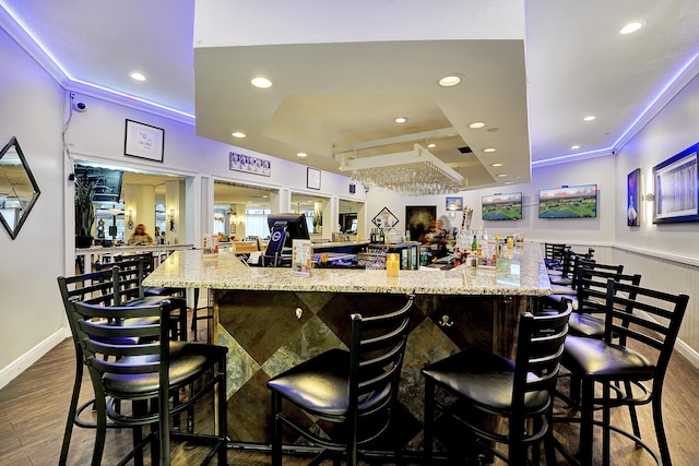 bar with a raised ceiling, light stone counters, ornamental molding, and hardwood / wood-style flooring