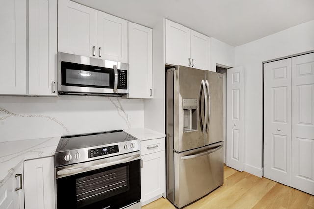 kitchen with white cabinets, light wood-type flooring, stainless steel appliances, and light stone countertops