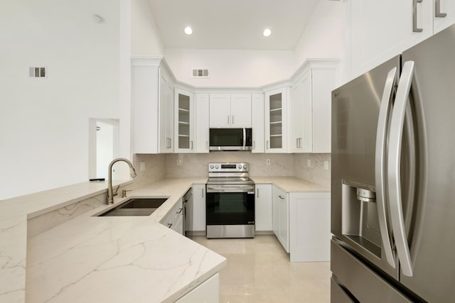 kitchen with white cabinets, sink, light stone countertops, kitchen peninsula, and stainless steel appliances