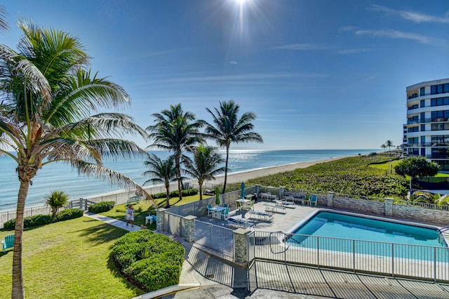 view of swimming pool with a patio area, a yard, a water view, and a view of the beach